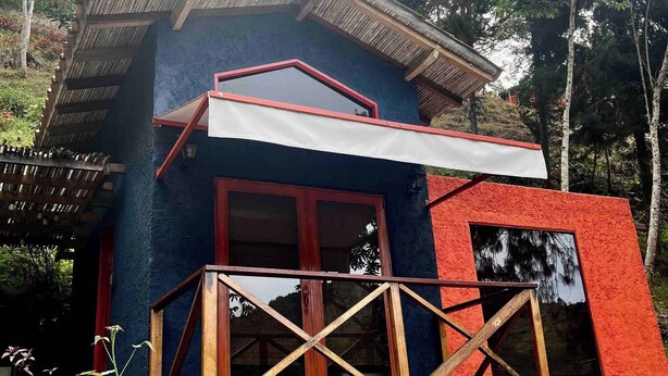 A small, two-story building with a balcony, surrounded by greenery and trees. - Casa Montserrat - Like From a Fairy Tale (Floridablanca)