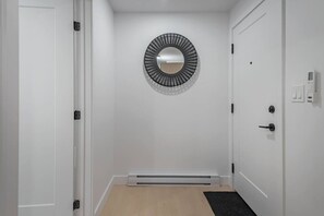 Ein Flur mit einer weißen Tür, einem runden Spiegel an der Wand und einer schwarzen Fußmatte.