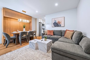 A modern living room with a grey sofa, a dining table with chairs, a white coffee table, and a kitchen in the background. - The Gerrard New Unit Near Fifa 2026 (Toronto)