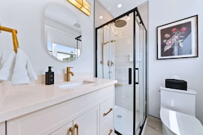 A modern bathroom with a glass shower enclosure, a white sink with gold handles, and a framed floral artwork on the wall. - The Gerrard New Unit Near Fifa 2026 (Toronto)