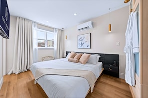 Une chambre d’hôtel moderne dotée d’un grand lit, d’une table de chevet, d’un climatiseur fixé au mur et d’une fenêtre avec des rideaux.