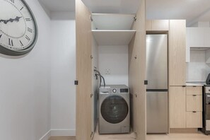 Eine kompakte Küche mit integrierter Waschmaschine und Trockner, einem Edelstahlkühlschrank und einer Wanduhr.