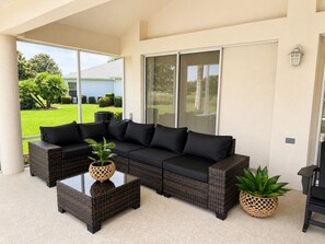 A covered patio area with a sectional sofa, two coffee tables, and potted plants. - Golf Course Retreat in The Villages with Water Views, Lanai & Prime Location (Lady Lake)