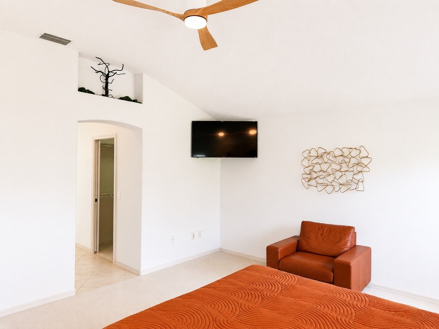 A modern living room with a ceiling fan, a flat-screen TV mounted on the wall, a brown leather chair, and a patterned rug.