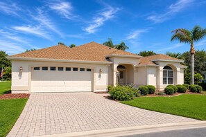 A single-story house with a garage, a front entrance with an archway, and a driveway leading to the garage. - Golf Course Retreat in The Villages with Water Views, Lanai & Prime Location (Lady Lake)