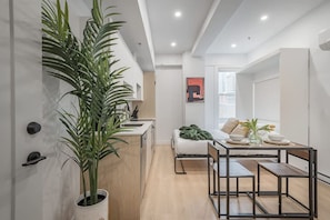 A modern kitchen with a dining area, a bed, and a large potted plant. - Light-Filled Studio Escape (Montréal)