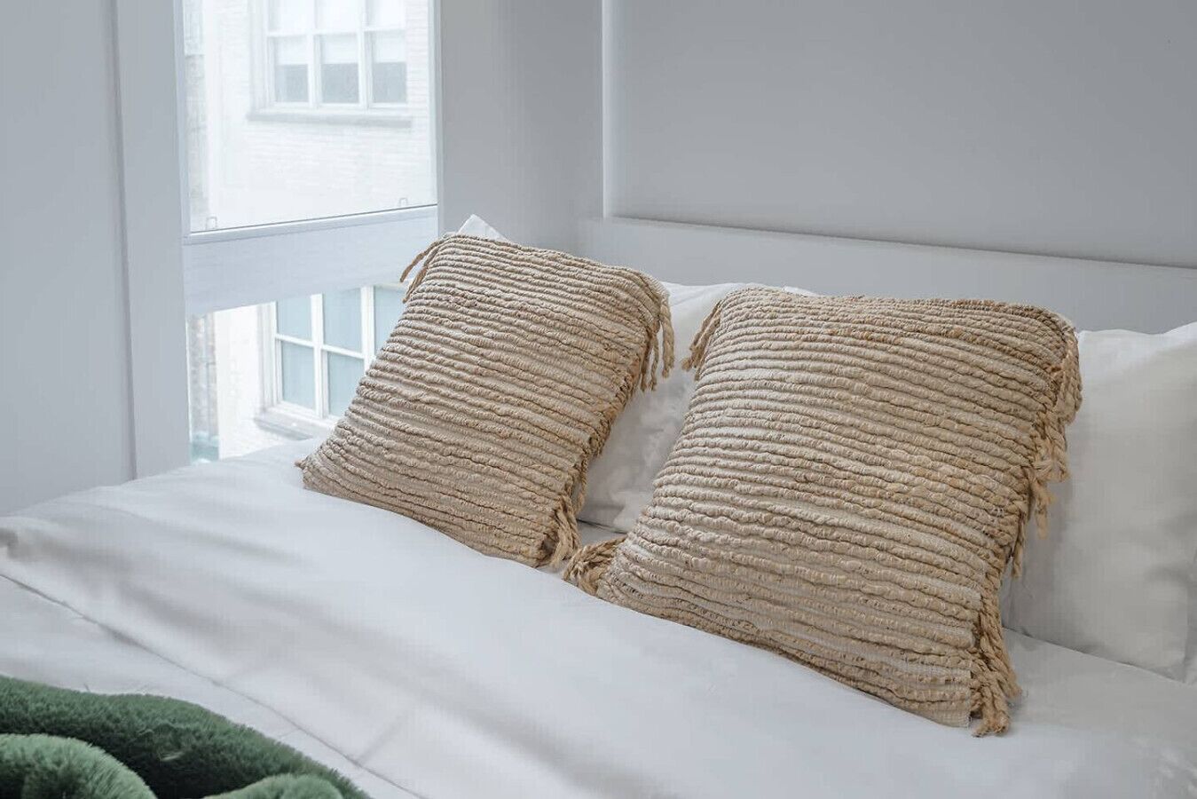 Un lit avec deux oreillers à texture et un plaid vert.