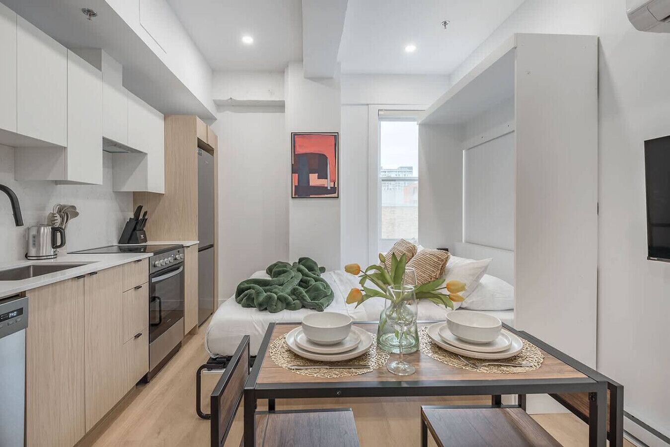 Une cuisine compacte dotée d’appareils électroménagers modernes, un coin repas avec une table dressée pour deux personnes, et un coin salon confortable avec un canapé et des coussins.