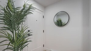 Un pasillo con una puerta blanca, una planta en maceta y un espejo redondo en la pared.
