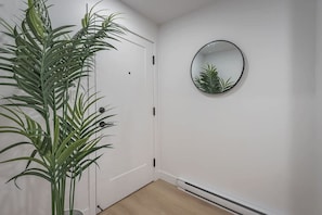 A hallway with a white door, a potted plant, and a round mirror on the wall.