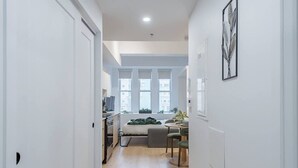 Un estrecho pasillo que conduce a un dormitorio con cama, escritorio y ventana.