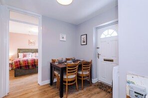 Una habitación con una cama, una mesa de comedor con sillas, una puerta blanca y una ventana.