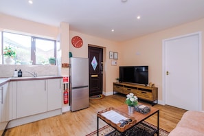 Un espacio habitable compacto con cocina, comedor, televisor y una puerta con un espejo decorativo en forma de diamante.