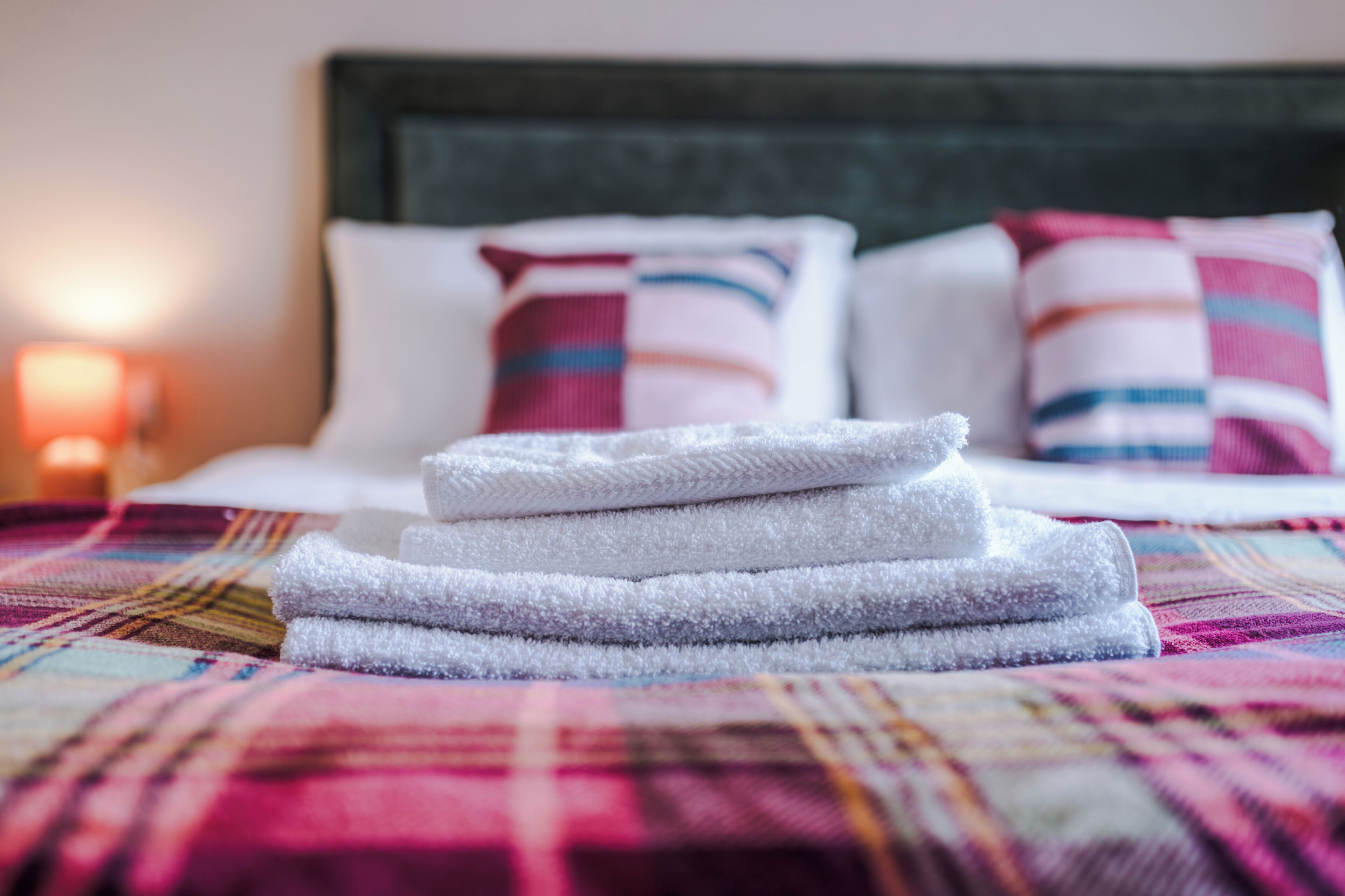 A bed with a colorful blanket, white pillows, and a stack of folded towels.