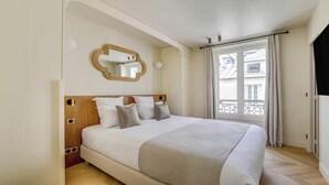 Una habitació d'hotel amb un llit gran, un panell de fusta al capçal, un mirall i una finestra amb cortines.