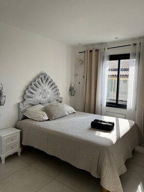 A bedroom with a large bed, a nightstand, a wall-mounted lamp, and a window with curtains. - Romantic villa for 6 near the sea with private pool (Fréjus)