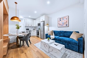Une cuisine moderne avec des meubles blancs, un canapé bleu et un coin repas comprenant une table et des chaises en marbre.