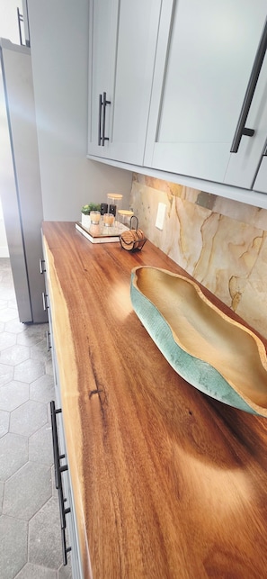 A kitchen with a wooden countertop, a marble backsplash, and a sink with a green interior.