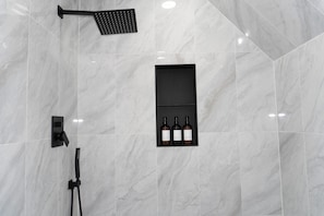 A bathroom with a shower, a wall-mounted shelf with bottles, and a tiled floor.