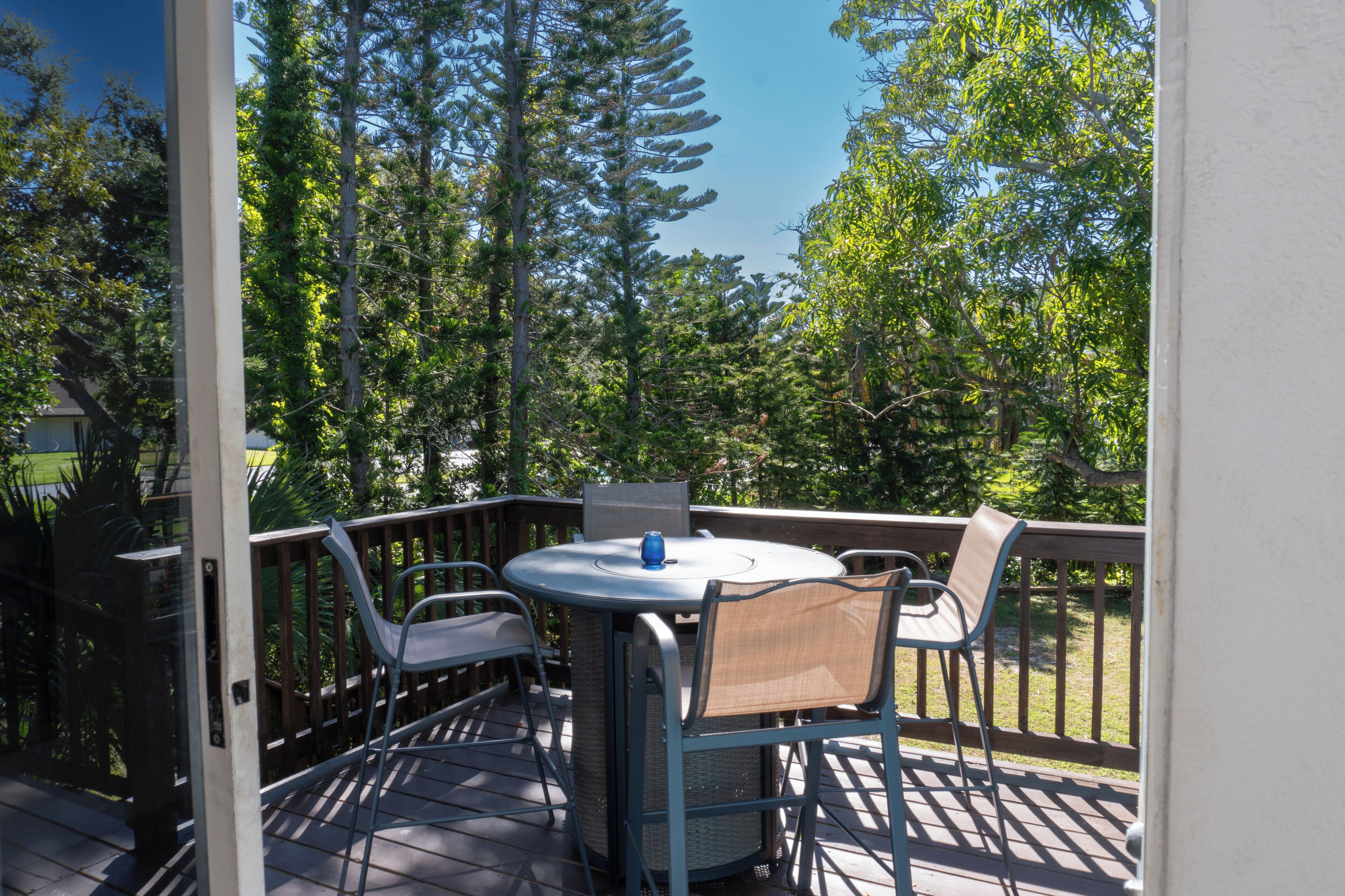 Une terrasse dotée d’une table ronde et de chaises, entourée d’une rambarde en bois, et offrant une vue sur une zone boisée.