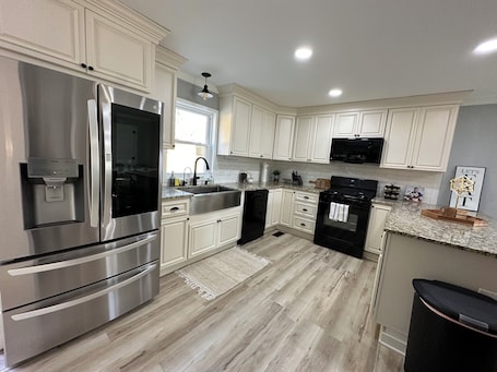 A kitchen with stainless steel appliances, white cabinetry, a granite countertop, and a wooden floor.. Queens place, sleeps 12