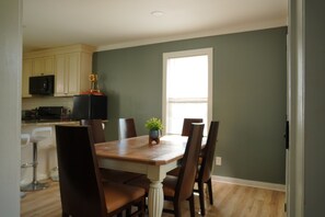 A dining area with a wooden table, six chairs, a potted plant, and a window. - Queens place, sleeps 12 (Raleigh)
