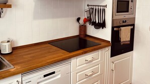 A modern kitchen with white cabinetry, a wooden countertop, a built-in dishwasher, a microwave, and a hanging light fixture. - Casa Serendipia in the heart of Riaza. (Riaza)