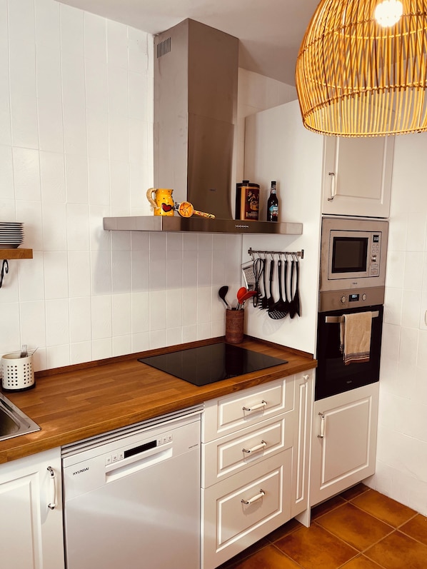 Eine moderne Küche mit weißen Schränken, einer Holz Arbeitsplatte, einem eingebauten Geschirrspüler, einer Mikrowelle und einer Pendelleuchte.