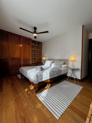 A bedroom with a wooden bed, a ceiling fan, a bedside table with a lamp, and a large wardrobe. - Casa Serendipia in the heart of Riaza. (Riaza)