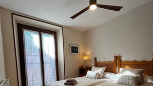 Une chambre d’hôtel avec deux lits, un ventilateur de plafond, une table de chevet avec une lampe et une fenêtre avec des rideaux.