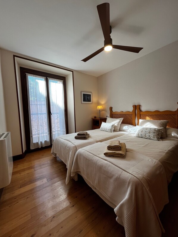 A hotel room with two beds, a ceiling fan, a nightstand with a lamp, and a window with curtains.