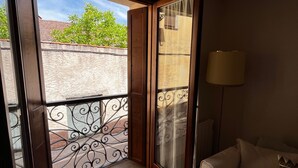 Une chambre d’hôtel avec un lit, une fenêtre donnant sur un immeuble et des arbres, une lampe et un ventilateur de plafond.