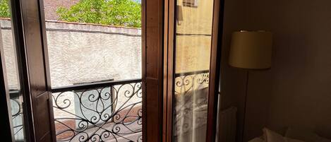 Ein Hotelzimmer mit Bett, Fenster mit Blick auf ein Gebäude und Bäume, einer Lampe und einem Deckenventilator.
