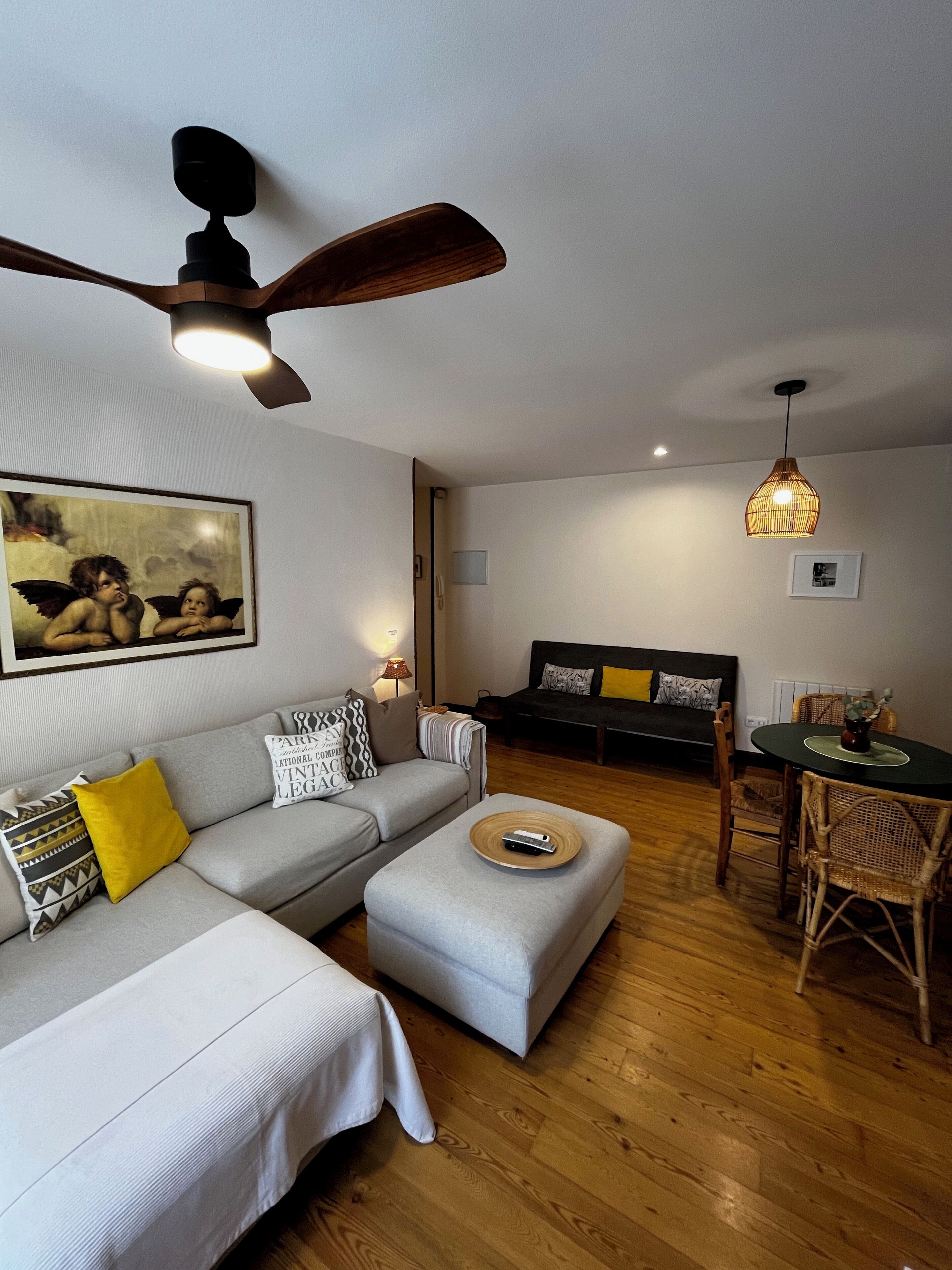 Una sala de estar moderna con un sofá gris, una mesa de comedor de madera y un ventilador de techo.