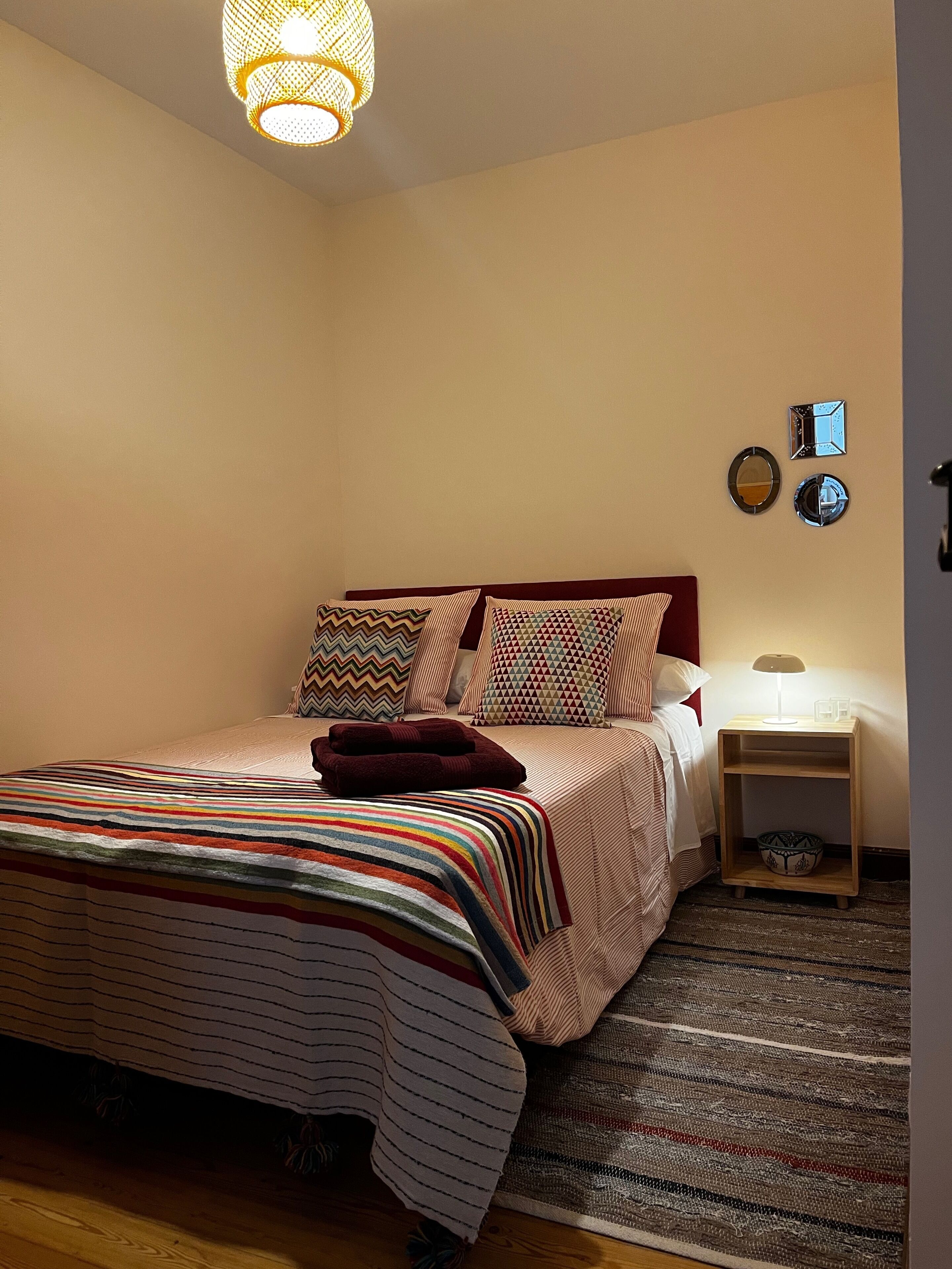 Une chambre à coucher avec un lit, des oreillers, une table de chevet, une lampe et une horloge murale.