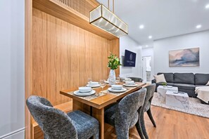 Un coin repas moderne avec une table en bois dressée pour quatre personnes, entourée de chaises rembourrées. Une plante en pot et un panneau encadré sont posés sur la table.