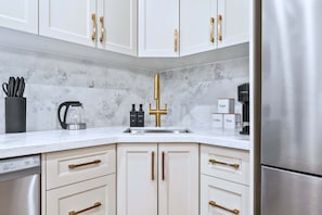 Una cocina moderna con armarios blancos, tiradores dorados, un refrigerador de acero inoxidable y una cafetera.