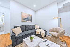 Un salon moderne avec un canapé gris, une table basse ronde, un fauteuil beige et un lampadaire.