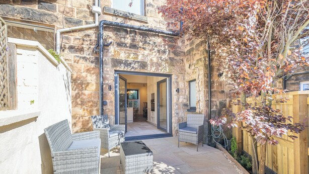 A stone building with a patio area featuring wicker furniture and a wooden fence.
