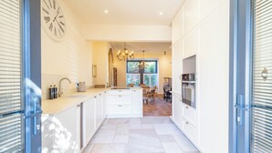 A modern kitchen with white cabinetry, a central island, a clock on the wall, and a dining area in the background.