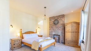 A bedroom with a wooden bed, a brick wall, a fireplace, and wooden furniture.