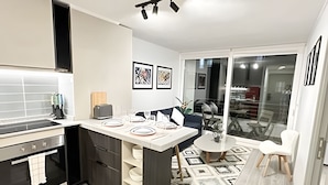 A modern kitchen with a central island, a dining area with a round table, and a view of the outside through a glass door. - Depto. céntrico cerca Movistar Arena (Santiago)