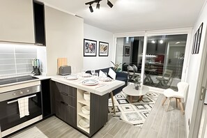 Een moderne keuken met een centraal eiland, een eethoek met een ronde tafel en uitzicht buiten door een glazen deur.