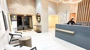 A modern reception area with a desk, chairs, and a glass door entrance. - Depto. céntrico cerca Movistar Arena (Santiago)