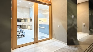 A hotel entrance with a sliding glass door, a tiled floor, and a visible interior space with a bed and a desk. - Depto. céntrico cerca Movistar Arena (Santiago)