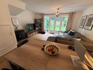 A living room with a wooden dining table, a laptop, a sofa, a television, and a bookshelf. -     Comfortable Family Home Near the River (Henley-on-Thames)