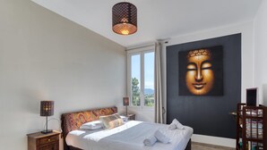 Une chambre à coucher avec un lit, une fenêtre, un tableau représentant un Bouddha, une table de chevet et une bibliothèque.