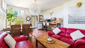 Un vaste espace de vie comprenant un canapé en cuir rouge, une table basse en bois et un coin repas avec des chaises en osier.