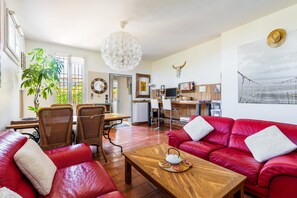 Un vaste espace de vie comprenant un canapé en cuir rouge, une table basse en bois et un coin repas avec des chaises en osier.