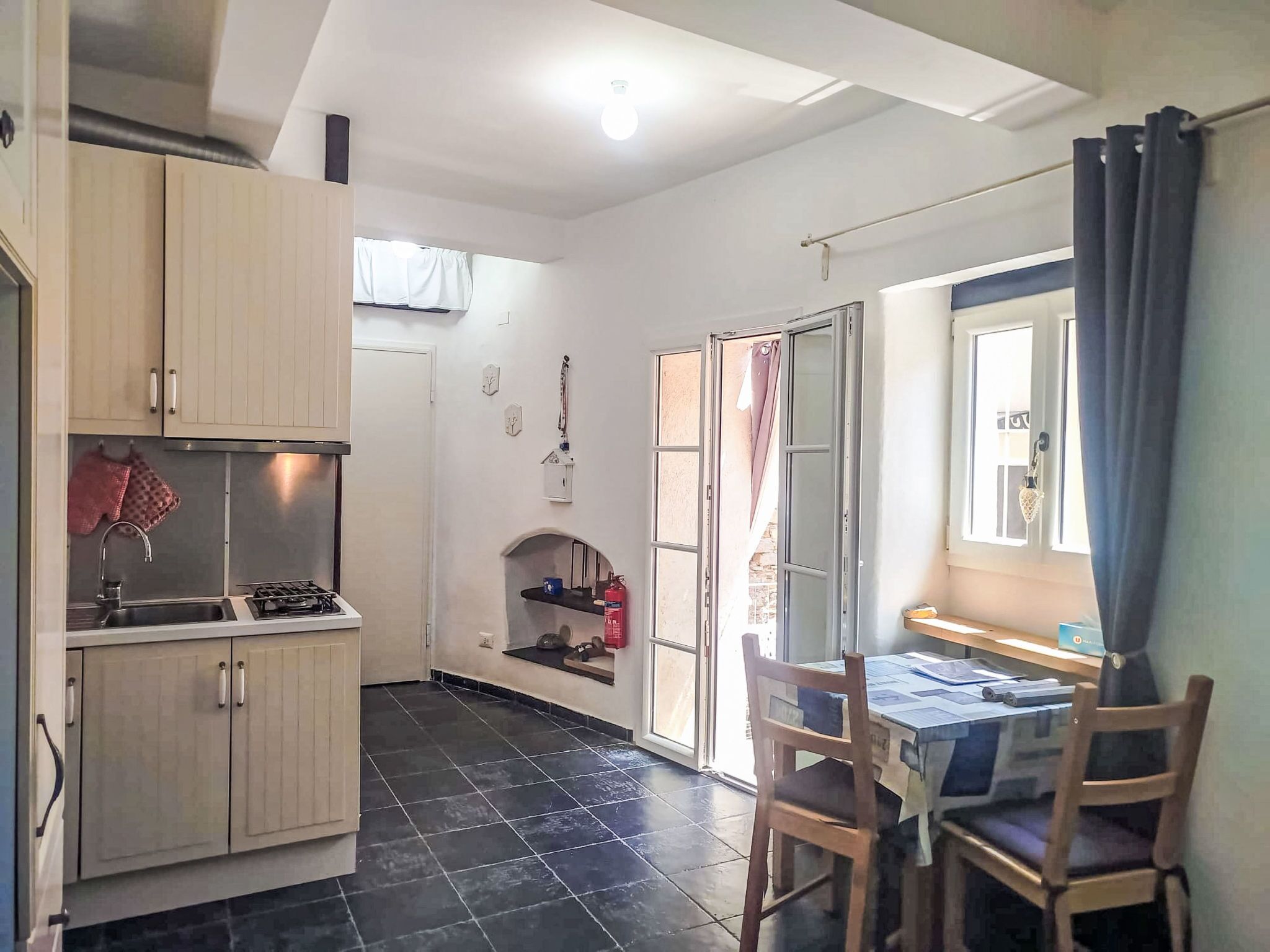 Een praktische keuken met een spoelbak, fornuis en kastjes, een eethoek met tafel en stoelen, en een raam met gordijnen.